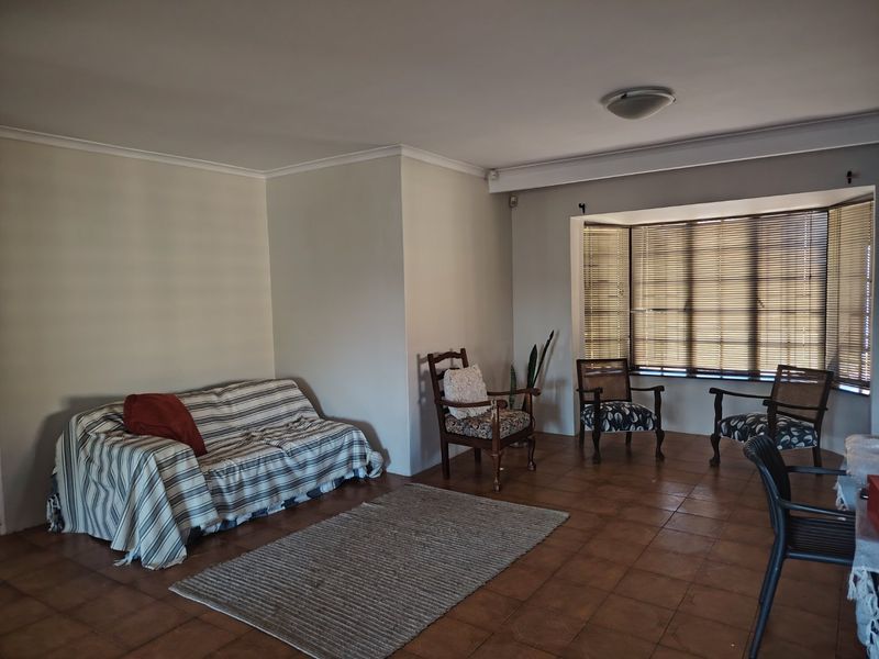 A spacious living room featuring tiled flooring, a large bay window with fitted venetian blinds, and neutral wall finishes.