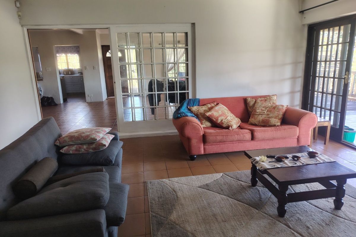 A spacious living room featuring tiled flooring and access to an outdoor area through glass sliding doors, with an adjacent room visible through french doors.