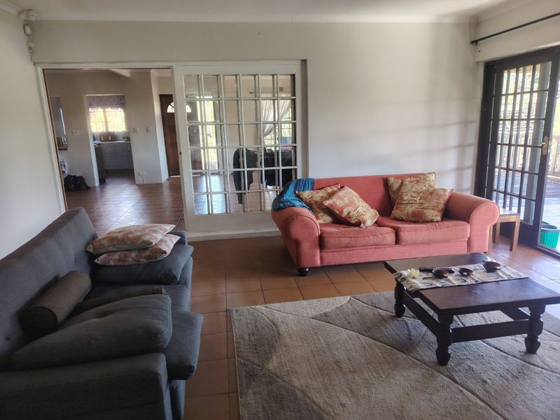A spacious living room featuring tiled flooring and access to an outdoor area through glass sliding doors, with an adjacent room visible through french doors.