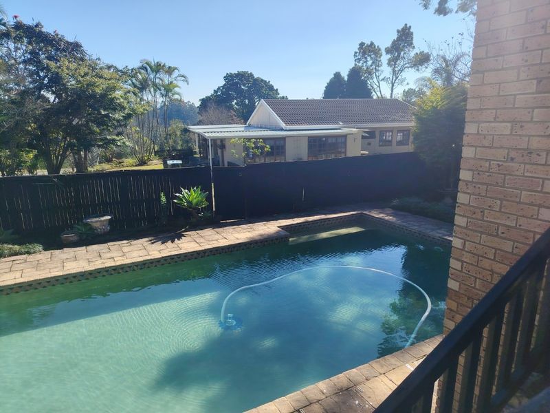 Outdoor swimming pool area featuring brick paving, a timber boundary fence, and views of the rear garden and neighboring property.