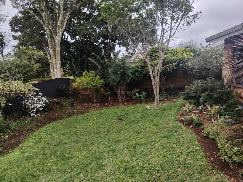A private rear garden featuring a manicured lawn, established trees, and landscaped garden beds enclosed by a brick boundary wall.