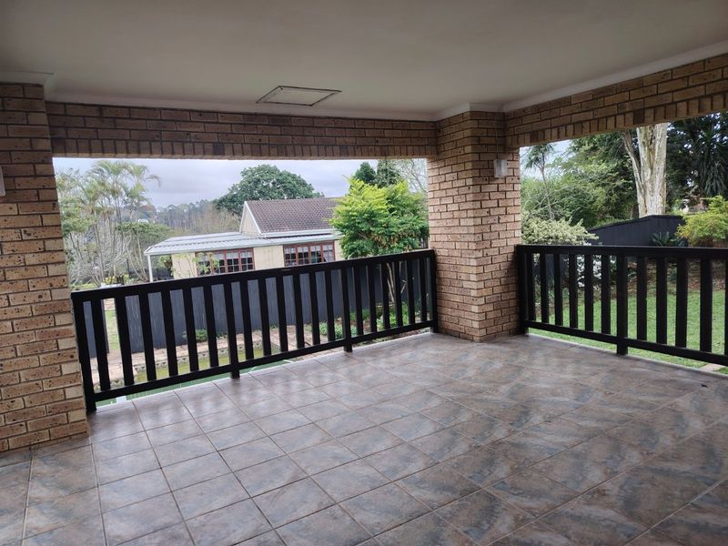 A covered outdoor patio featuring face brick pillars, tiled flooring, and a timber balustrade overlooking the garden.