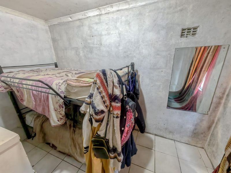 A compact bedroom featuring tiled flooring and a wall-mounted mirror, requiring cosmetic updates to improve the overall condition of the wall finishes.