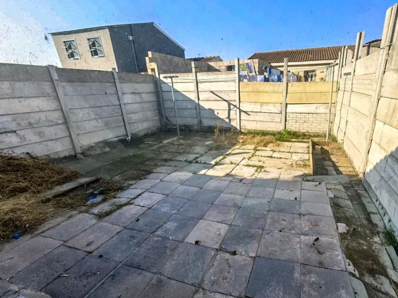 A rear courtyard area featuring a paved patio enclosed by precast concrete boundary walls, offering a blank canvas for landscaping and outdoor improvement.