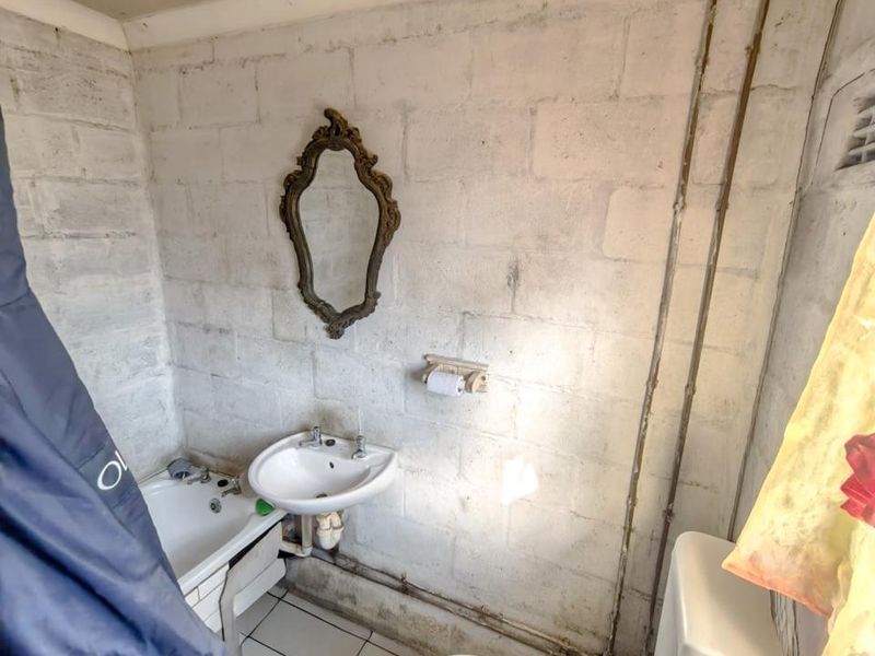 A small bathroom featuring a pedestal basin, toilet, and bathtub with exposed pipework and unfinished blockwork walls in need of renovation.