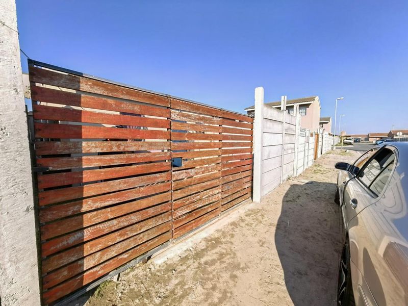 Front boundary view featuring a timber slat gate and precast concrete walling along an unpaved street verge.