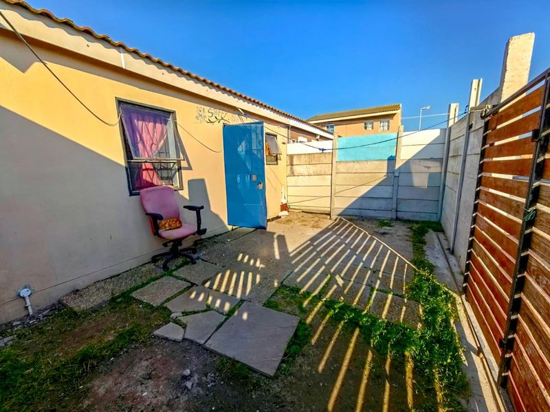 A rear exterior courtyard featuring a paved patio area, enclosed by precast concrete boundary walls and a side gate.