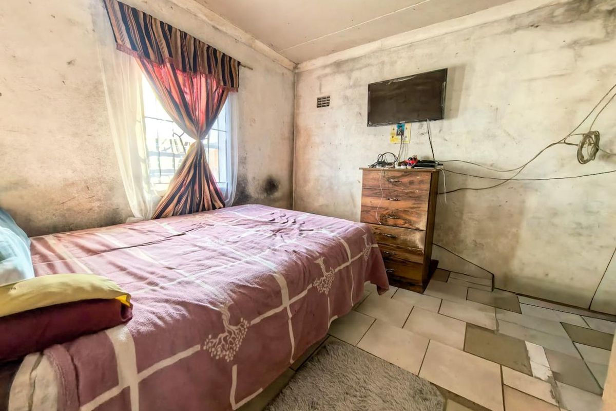 A bedroom featuring tiled flooring and a window with security bars, currently requiring significant wall repairs and cosmetic renovation.