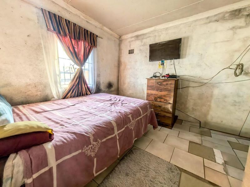 A bedroom featuring tiled flooring and a window with security bars, currently requiring significant wall repairs and cosmetic renovation.