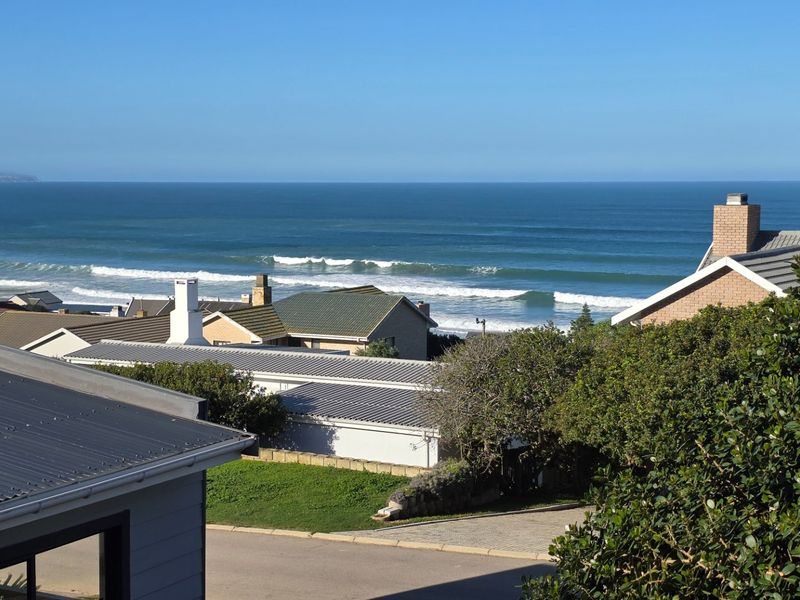 Elevated coastal view overlooking neighbouring residential rooftops towards the ocean.