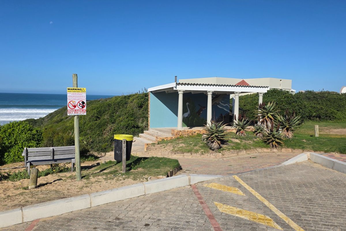 An outdoor covered patio area overlooking the coastline, featuring concrete columns and adjacent paved parking space.