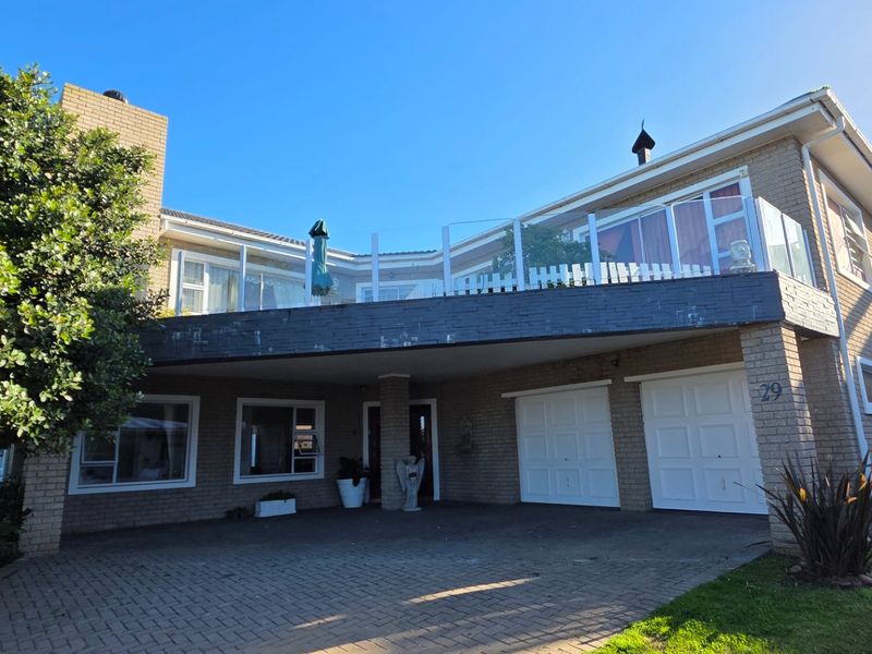 Front elevation of a double-story brick house featuring a paved driveway, double garage, and an upper-level balcony with a glass balustrade.