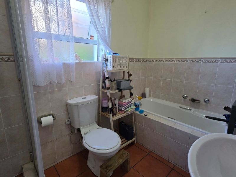 A functional bathroom featuring a built-in bathtub, shower enclosure, toilet, and basin with neutral wall tiling and terracotta floor tiles.