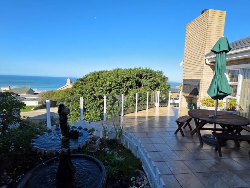 Spacious outdoor patio featuring tiled flooring, a built-in brick fireplace, and a glass balustrade with scenic ocean views.