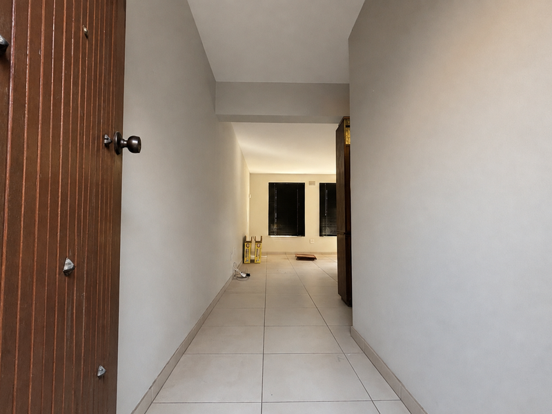 A clean, neutral-toned entrance hallway featuring tiled flooring and a solid timber front door, leading into an open-plan living area.