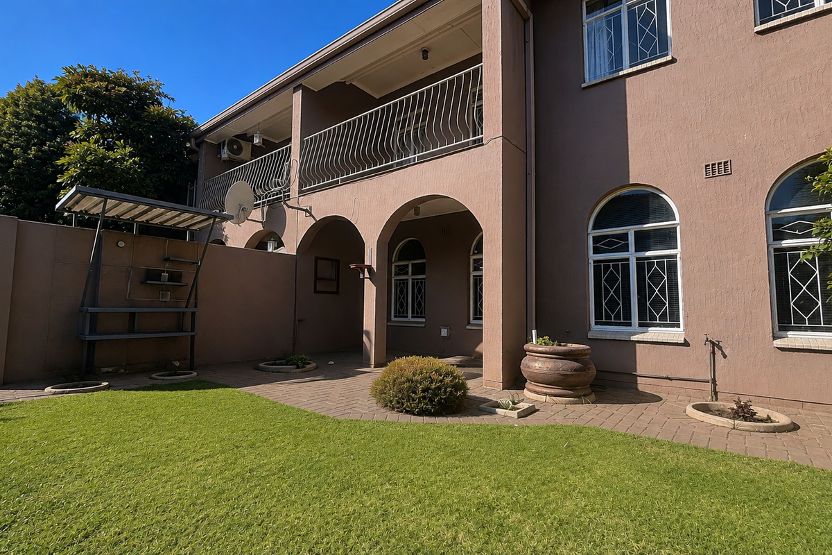 Rear view of the townhouse featuring a paved patio area, arched architectural details, an upper-level balcony with wrought iron railing, and a well-maintained garden.