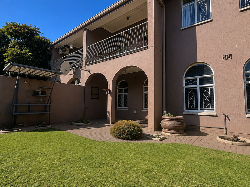 Rear view of the townhouse featuring a paved patio area, arched architectural details, an upper-level balcony with wrought iron railing, and a well-maintained garden.