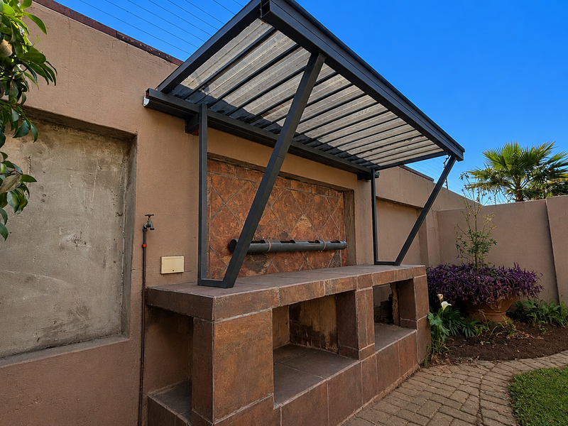 Outdoor entertainment area featuring a built-in braai with tiled finishes, a metal pergola structure, and a paved garden walkway.