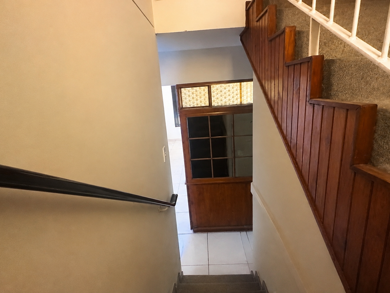 A staircase hallway featuring wooden wall paneling, a wooden balustrade, and tiled flooring leading to a glass-paneled door.