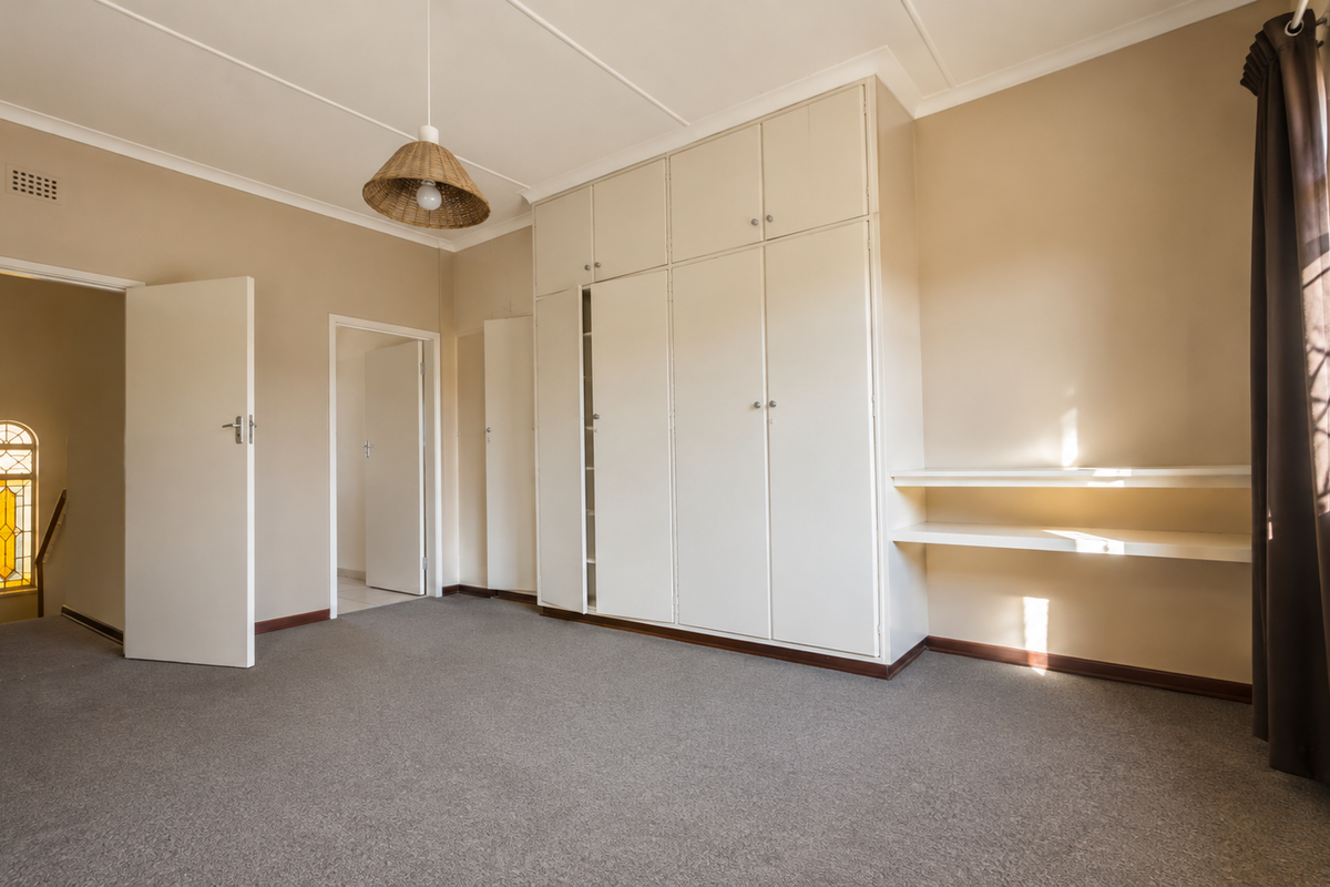 Spacious bedroom featuring neutral walls, carpeted flooring, extensive built-in cupboard storage, and a charming leaded glass window detail.