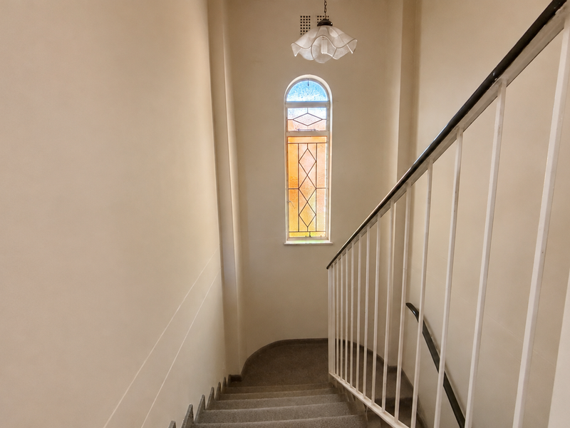 A bright staircase landing featuring a decorative stained glass window and a simple metal balustrade.
