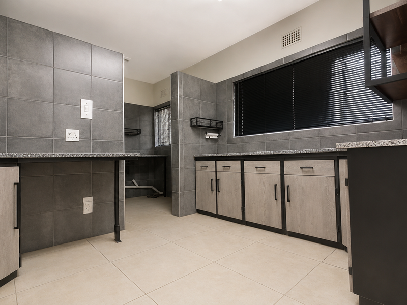 A modern, well-maintained scullery featuring grey cabinetry, granite countertops, and tiled walls, providing ample storage and dedicated space for laundry or kitchen prep.