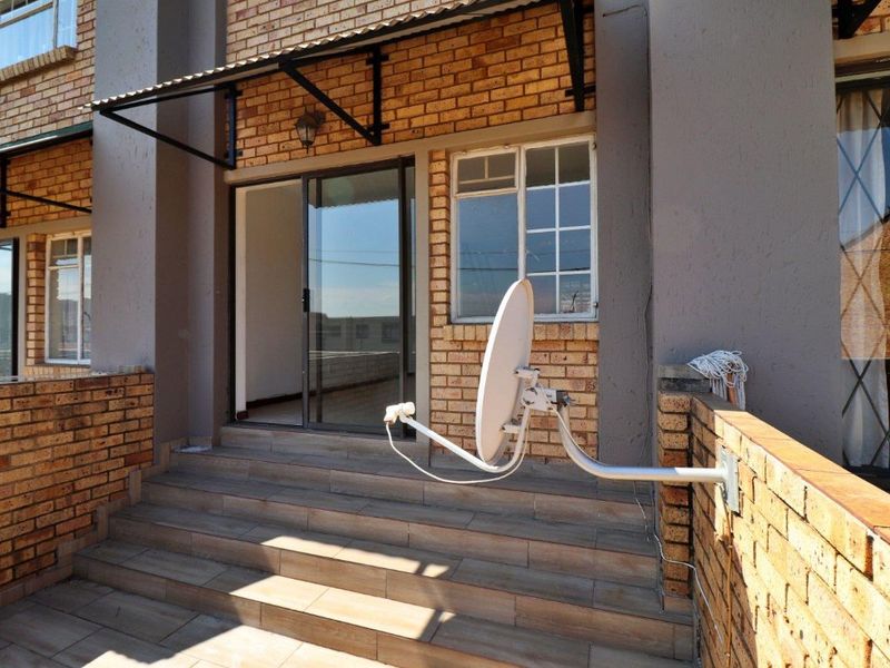 A paved outdoor patio area featuring a brick facade, sliding glass door access, and a mounted satellite dish.