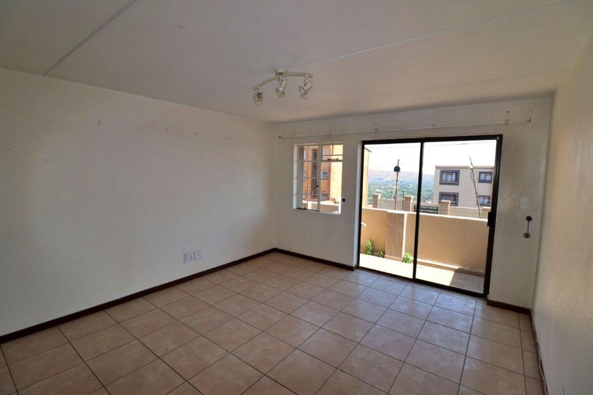 An empty living room featuring tiled flooring, a ceiling spotlight fixture, and a sliding glass door providing access to an outdoor balcony area.