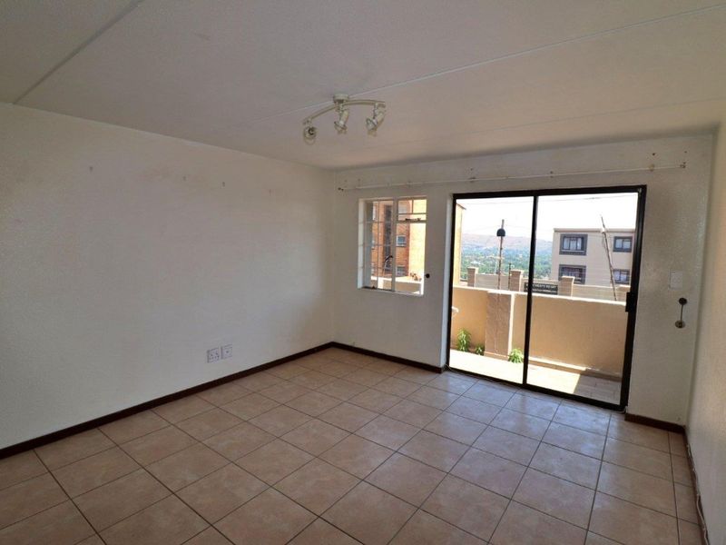 An empty living room featuring tiled flooring, a ceiling spotlight fixture, and a sliding glass door providing access to an outdoor balcony area.