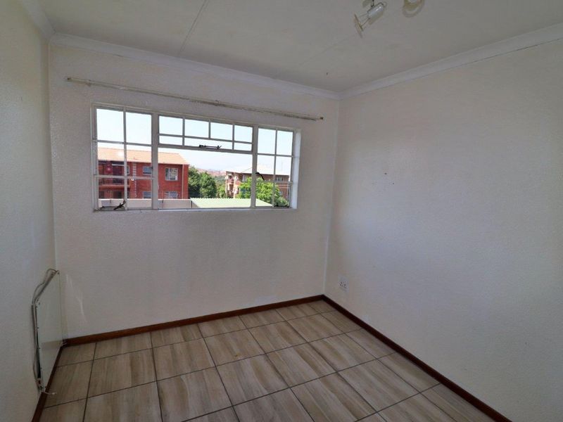 An empty bedroom featuring tiled flooring, a steel-framed window, and a wall-mounted heater, offering a blank canvas for personalization.