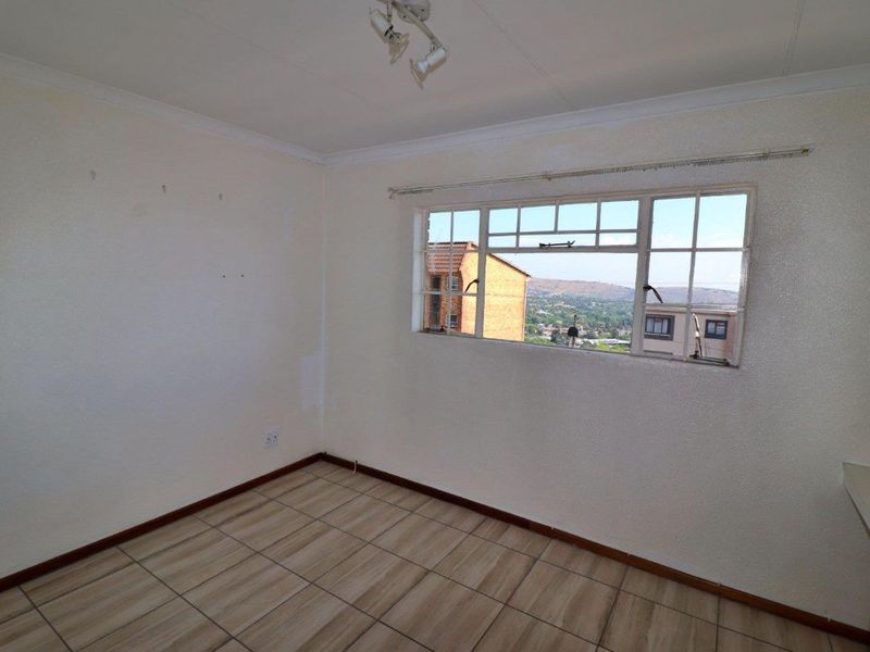 An empty bedroom featuring tiled flooring, a steel-framed window with exterior views, and coved ceilings. The walls show signs of wear and patch repairs.