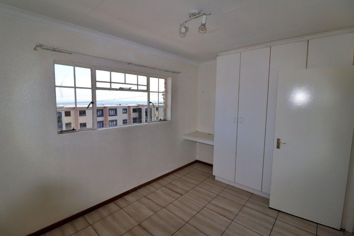 An empty bedroom featuring tiled flooring, built-in cupboards, a built-in desk, and a steel-framed window with views of the surrounding neighborhood.