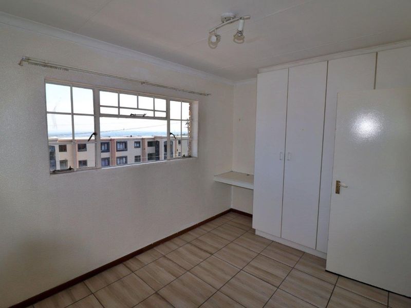 An empty bedroom featuring tiled flooring, built-in cupboards, a built-in desk, and a steel-framed window with views of the surrounding neighborhood.