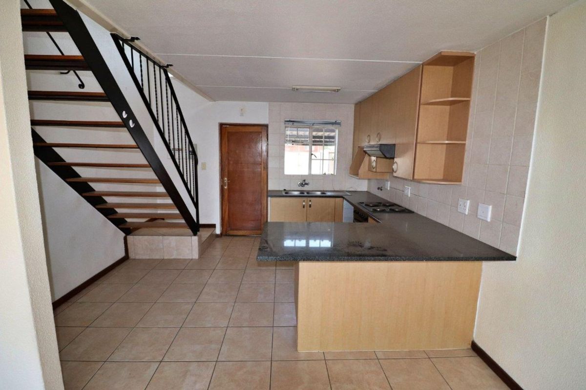 Open-plan kitchen featuring granite countertops, built-in cabinetry, and a tiled backsplash, conveniently located adjacent to the staircase.