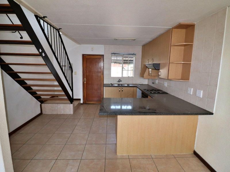 Open-plan kitchen featuring granite countertops, built-in cabinetry, and a tiled backsplash, conveniently located adjacent to the staircase.
