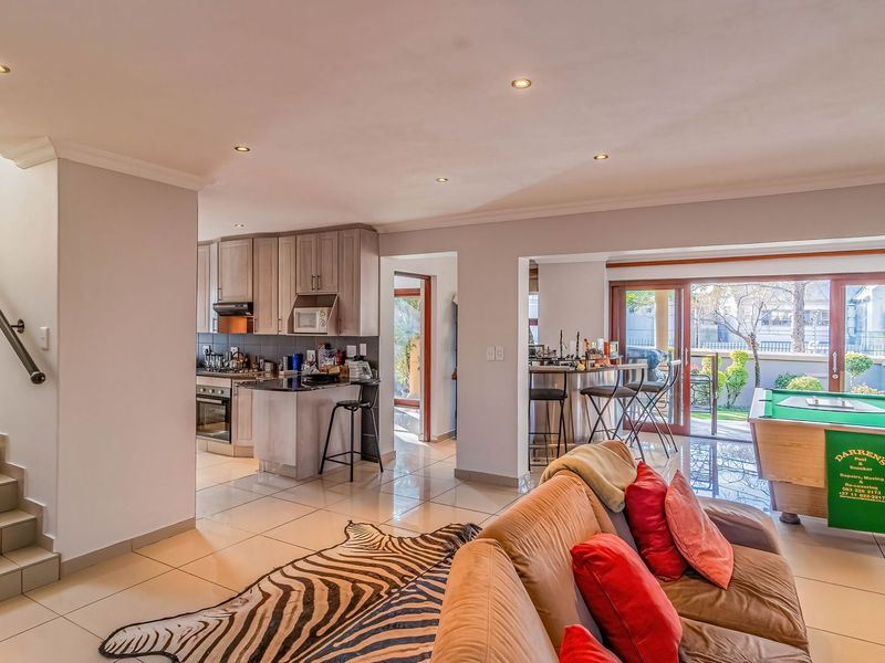 Spacious open-plan living area featuring tiled floors, a modern kitchen with built-in appliances, a staircase, and sliding doors leading to the outdoor patio.