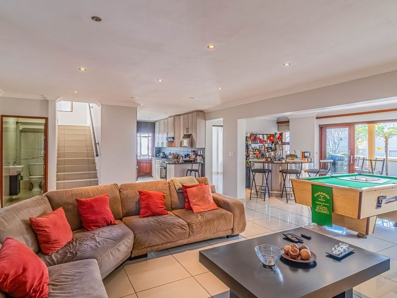 Spacious open-plan living area featuring tiled floors, recessed lighting, a built-in bar, and a modern kitchen, with direct access to the outdoor patio.