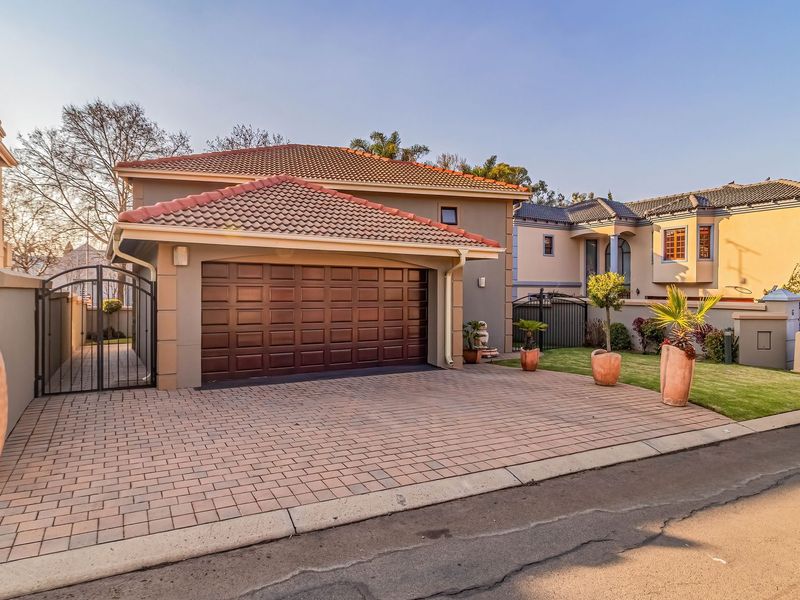 Front elevation of a residential property featuring a paved driveway, double garage, and well-maintained boundary wall with gated access.