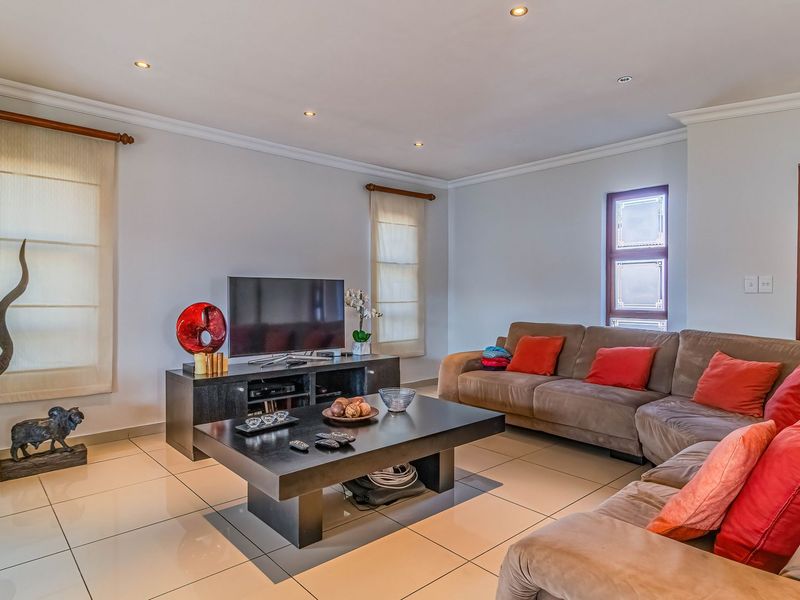 A well-maintained living room featuring polished porcelain floor tiles, recessed downlighting, and decorative cornicing, creating a bright and comfortable living space.