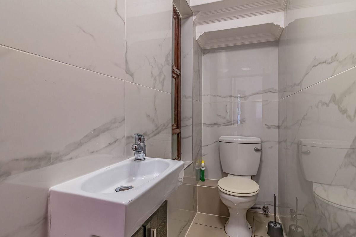 A compact, modern bathroom featuring marble-look wall tiles, a wall-mounted basin, and a standard toilet with crown molding detailing.