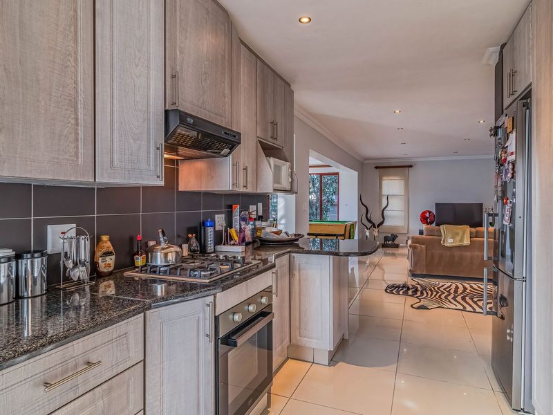 Modern open-plan kitchen featuring granite countertops, built-in oven, gas hob, and sleek cabinetry, flowing seamlessly into the adjacent living area with tiled flooring.