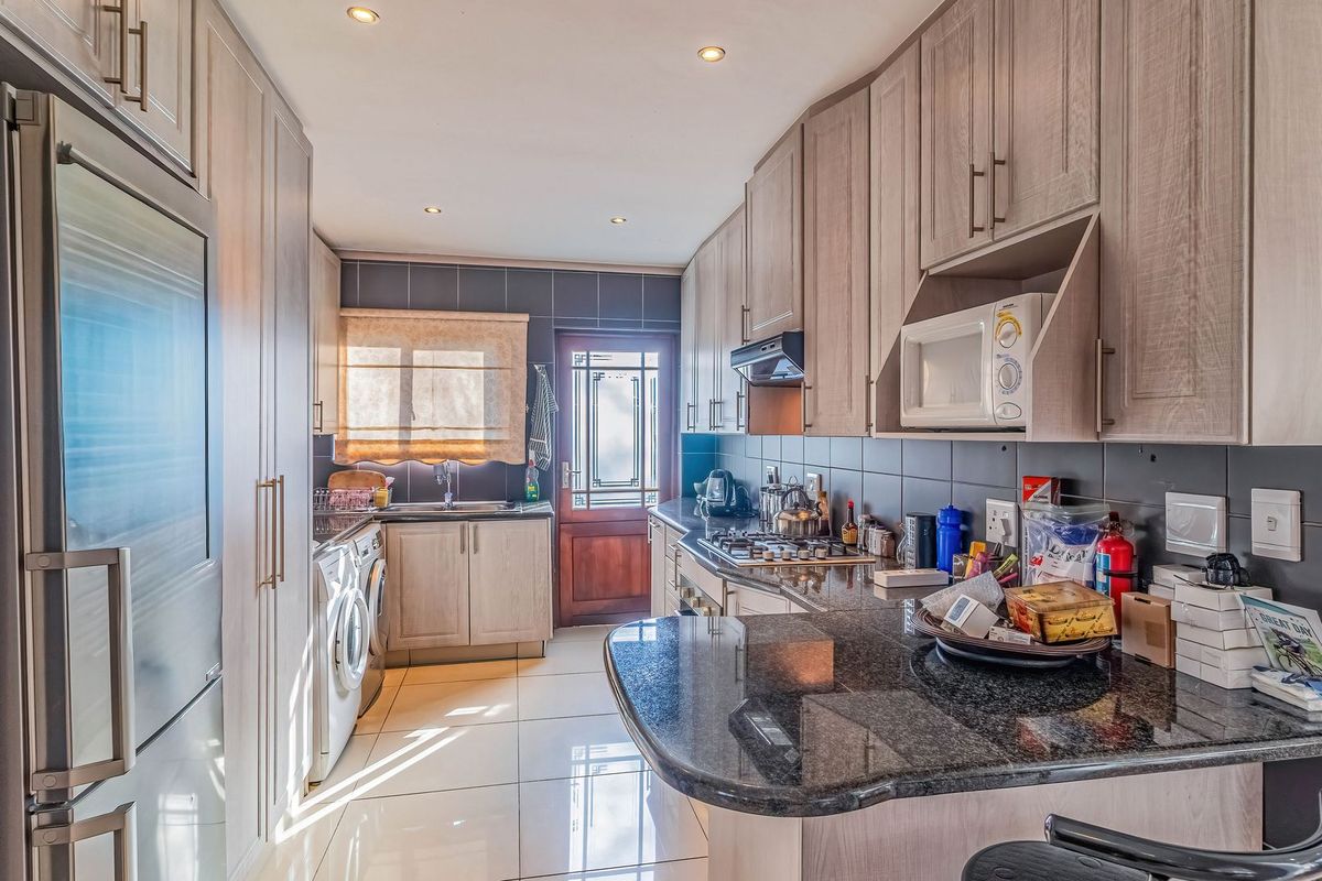 A functional kitchen featuring light wood cabinetry, granite countertops, a gas hob, and integrated appliances with tiled flooring and direct exterior access.