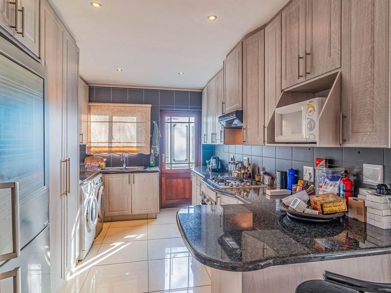 A functional kitchen featuring light wood cabinetry, granite countertops, a gas hob, and integrated appliances with tiled flooring and direct exterior access.