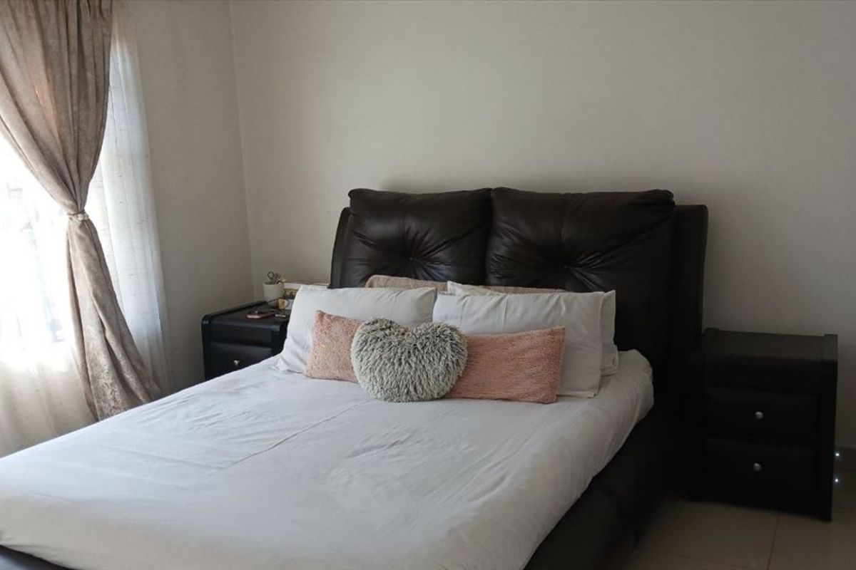 A standard bedroom featuring tiled flooring and a window fitted with security bars, providing a functional and private sleeping space.
