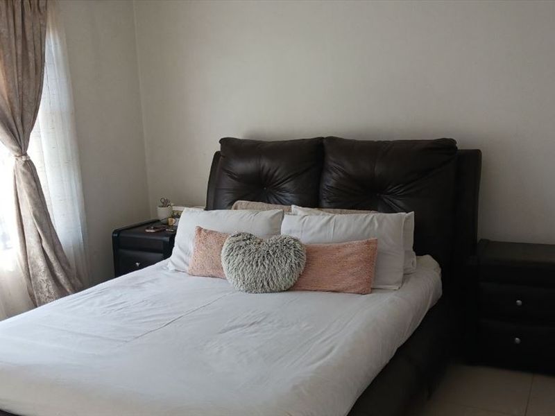 A standard bedroom featuring tiled flooring and a window fitted with security bars, providing a functional and private sleeping space.