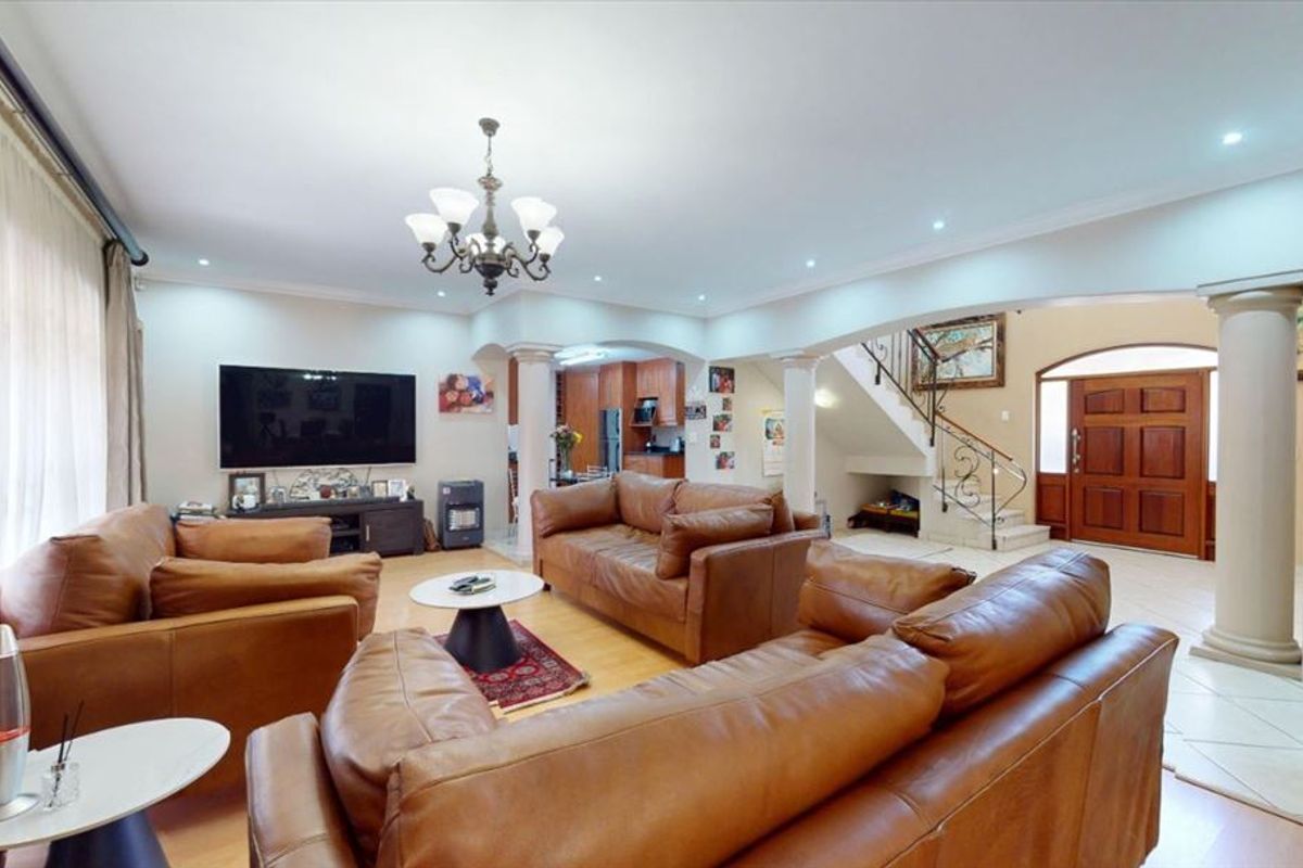 Spacious open-plan living area featuring elegant columns, an arched entryway, a staircase with wrought iron detailing, and a mix of laminate and tiled flooring.