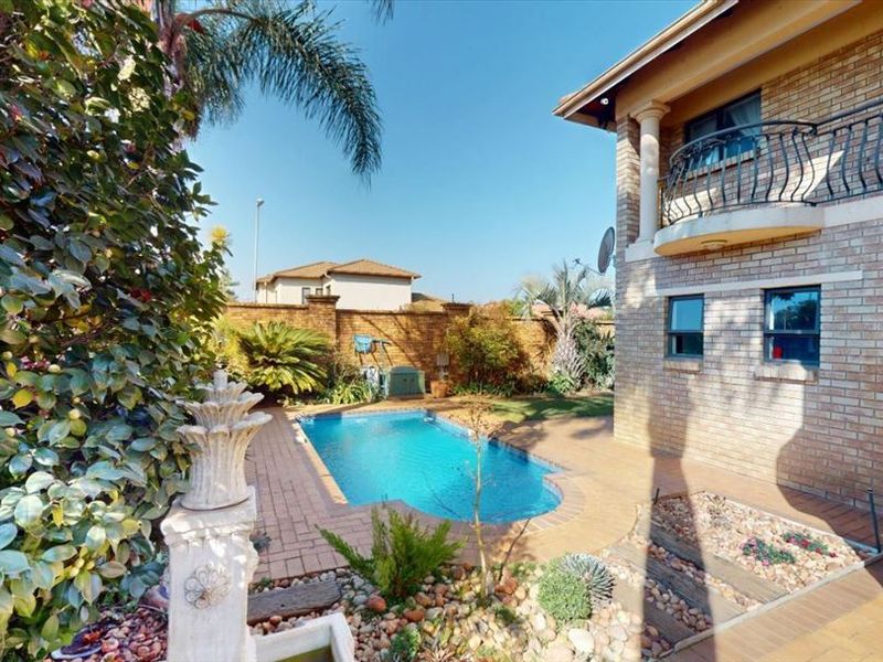 Outdoor pool area featuring a swimming pool, brick paving, and a brick boundary wall, adjacent to the townhouse facade with a balcony.