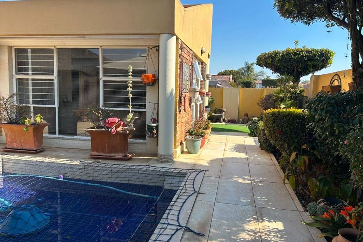 A well-maintained outdoor pool area featuring a tiled patio, brick facade, and sliding glass doors leading into the townhouse.