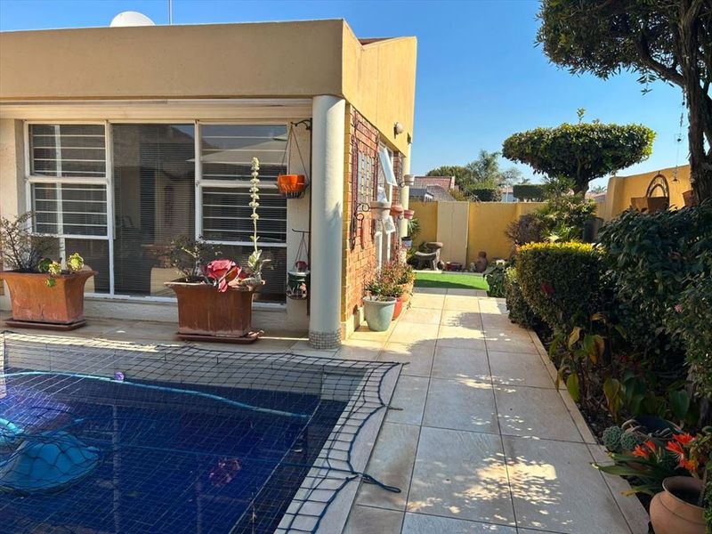 A well-maintained outdoor pool area featuring a tiled patio, brick facade, and sliding glass doors leading into the townhouse.