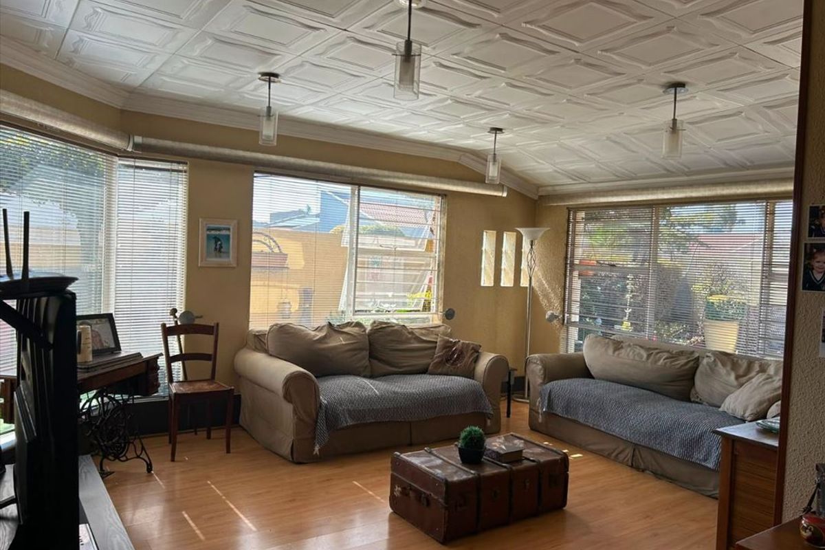 Spacious living room featuring laminate flooring, a distinctive coffered ceiling, and large windows with venetian blinds providing ample natural light.